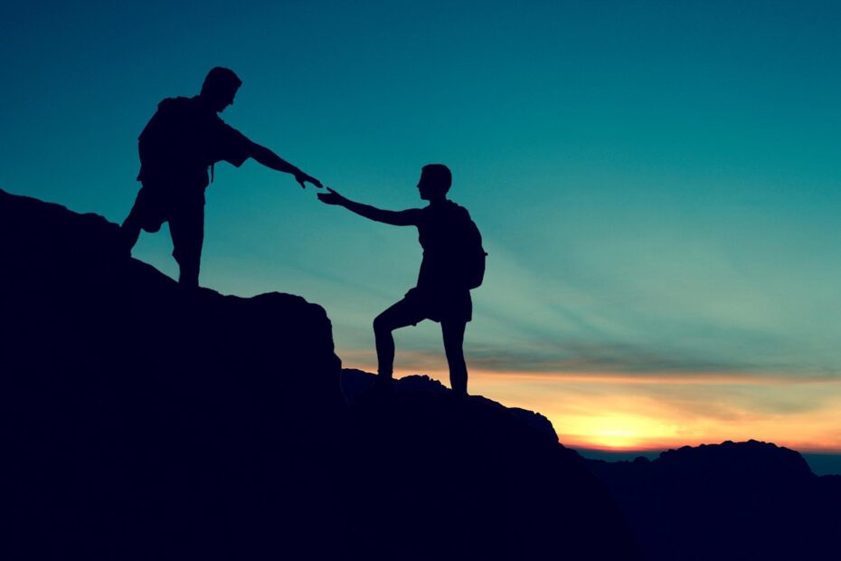 Das Bild zeigt zwei Silhouetten von Personen in einer Berglandschaft bei Sonnenuntergang. Eine Person steht auf einem höheren Felsen und reicht der anderen die Hand, um ihr zu helfen, nach oben zu kommen. Die Szene vermittelt ein starkes Gefühl von Unterstützung, Hilfsbereitschaft und Solidarität. Bezug zur Goldenen Regel: Goldene Regel Judentum: „Was dir verhasst ist, das tue deinem Nächsten nicht.“ (Talmud, Schabbat 31a) Goldene Regel Bibel: „Alles nun, was ihr wollt, dass euch die Leute tun sollen, das tut ihr ihnen auch.“ (Matthäus 7,12) Goldene Regel Ethik: Der Grundsatz, andere so zu behandeln, wie man selbst behandelt werden möchte, gilt als eine universelle ethische Maxime in vielen Religionen und Philosophien. Das Bild illustriert diese Prinzipien anschaulich durch die Geste des Helfens: Die Person auf dem Felsen hilft der anderen, anstatt sie zurückzulassen. Es symbolisiert Mitgefühl, Empathie und das Streben nach einem harmonischen Miteinander.